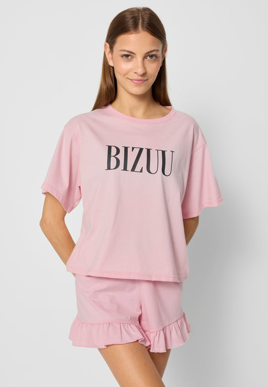 Modelka na tle białej ściany z rękoma z tyłu ubrana w różową piżamę z czarnym logo BIZUU.