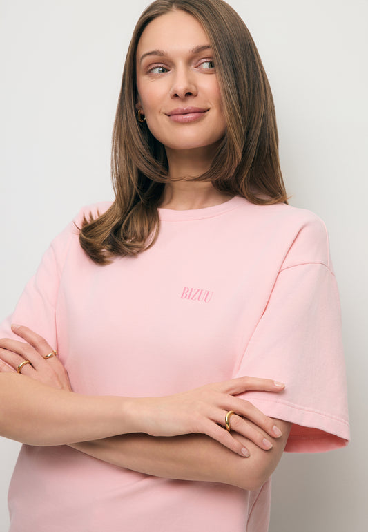 Zbliżenie na modelkę z założonymi rękoma ubraną w różowy T-shirt CLOUD z logo na przodzie.