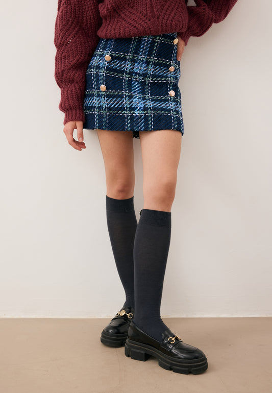 Zbliżenie na nogi modelki ubranej w mini spódniczkę w granatową kratę DISSA , podkolanówki SCHOOLI i buty lesotho.