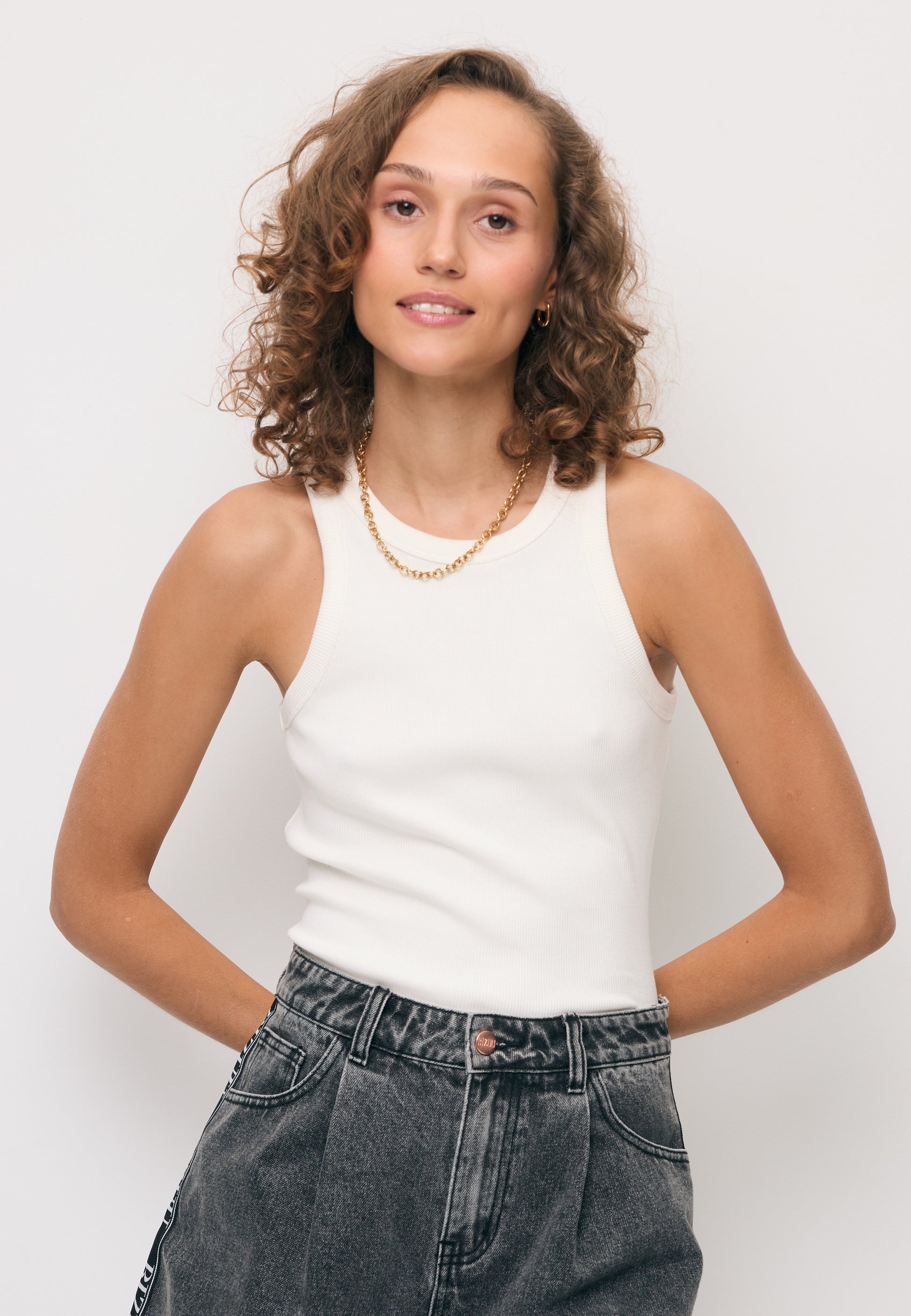 Modelka w prążkowanym topie z logo na plecach ALEXIN oraz jeansowych szortach MIREYA.