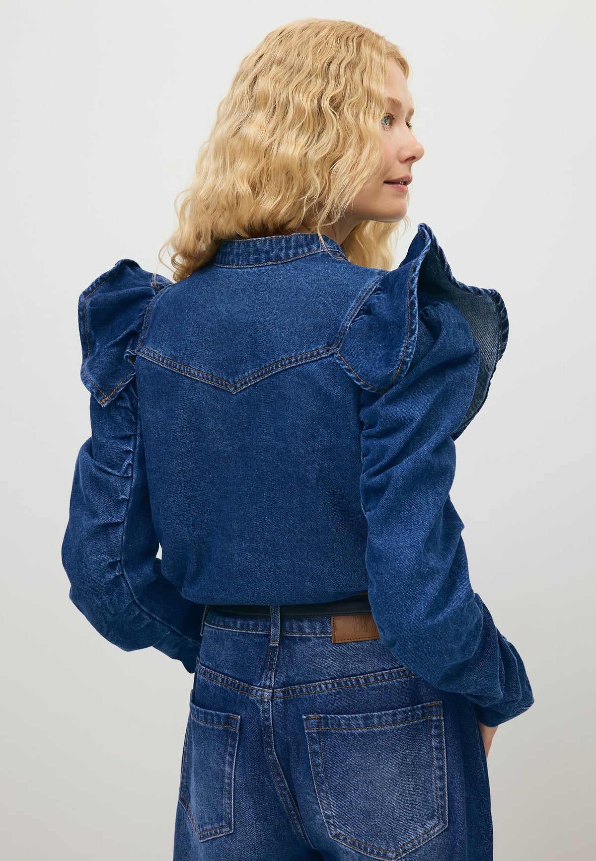 Modelka z jedną ręką w kieszeni granatowych jeansów LEYLA, ubrana w granatową koszulę jeansową DILETTA.