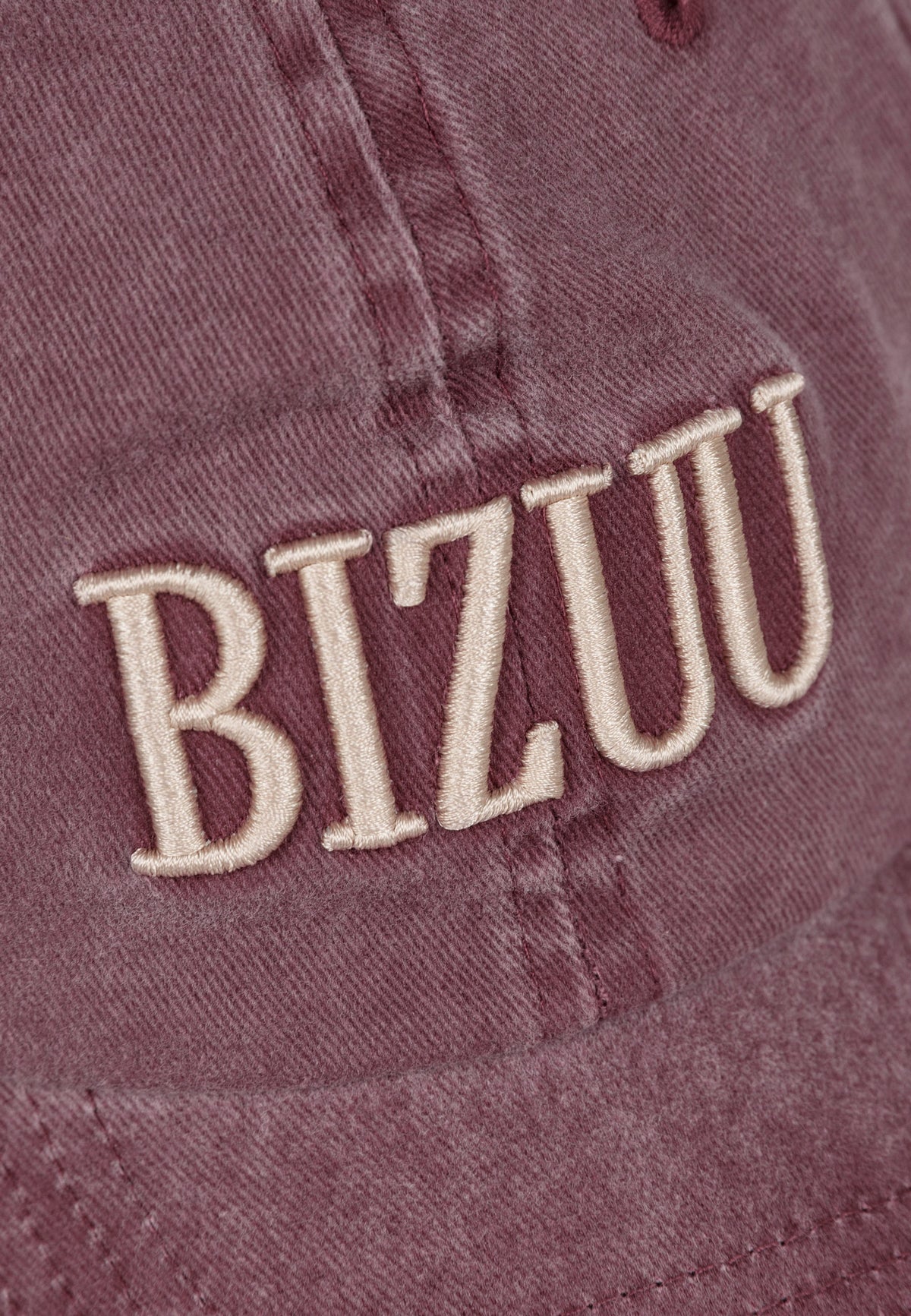 Zbliżenie na haftowane logo na przodzie bordowej czapki z daszkiem ZANE.
